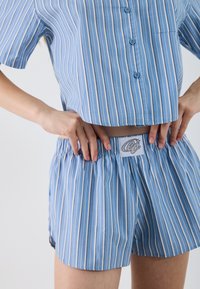 Short-sleeve blue and white striped top with buttons paired with matching elastic-waist shorts featuring a label on the waistband.