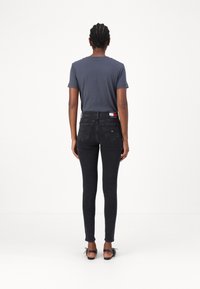 Tmavě modré džínové skinny džíny s vysokým pasem, zadními kapsami a páskem s logem značky. Kombinované se šedým bavlněným tričkem a černými botami.