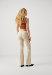 Pantalones acampanados beige con una textura suave, que cuentan con bolsillos traseros. Combinados con un top corto estampado en naranja y negro.