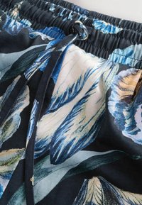 Gėlių maudymosi šortai tamsiai mėlynu fonu, su šviesiai mėlynomis ir grietinėlės spalvos lapų raštais. Reguliuojama raištelių juosta ir elastingas juosmuo.