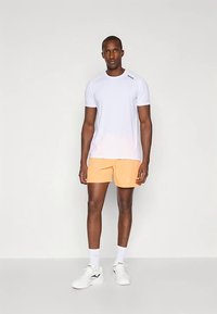 Camiseta branca de manga curta e calções desportivos laranja claro. O conjunto é complementado com sapatilhas brancas e meias até ao tornozelo.