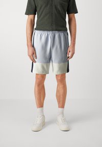 Shorts de sport bleu clair avec des rayures latérales bleu foncé et un panneau inférieur vert menthe. Associés à une chemise à manches courtes boutonnée vert foncé.