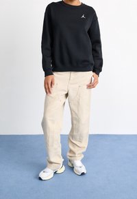 Sudadera negra con logo blanco, pantalones cargo beige y zapatillas blancas y azules. Tejido suave, ajuste relajado, costuras visibles y bolsillos en los pantalones.