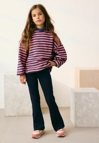 Stribet sweatshirt i pink og marineblå med brede ærmer, parret med marineblå buks med flared ben og lyserøde sneakers, sat mod en neutral baggrund.