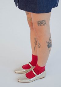 Sidabrinės Mary Jane avalynės su apvaliu nosiu, derinamos su raudonomis banguotomis kojinėmis. Išskirtiniai bruožai - kulkšnies dirželis ir plokščias padas.