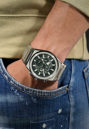 Silberner Edelstahl-Armbanduhr mit einem dunkelgrünen, gemusterten Zifferblatt, Chronographenfunktionen und einem verbundenen Metallarmband, das an einer Hand getragen wird.