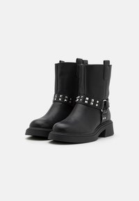 Bottes de cheville en cuir noir avec un talon épais, dotées d'une sangle cloutée en argent et de languettes sur le côté pour un enfilage facile. Texture lisse, design robuste.