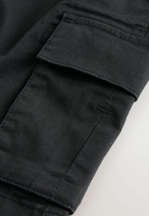 Mustad kaubapükste kangas, millel on suur kaubatasku õmmeldud detailidega. Materjal on sile, veidi läikiva pinnaga ja vastupidava tekstuuriga.