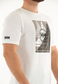 Camiseta de algodón blanca de manga corta, con un gráfico geométrico en negro y gris y el logo "HH" en la manga.