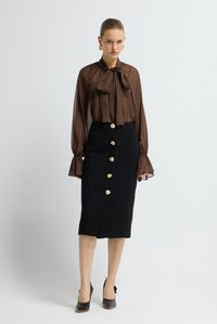Hnědá průsvitná halenka s mašlí a rozšířenými rukávy, doplněná černou pouzdrovou sukní se zlatými květinovými knoflíky a bočními kapsami.