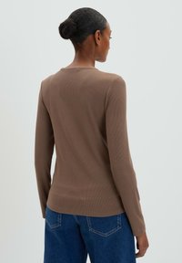 Top a maniche lunghe marrone a coste con scollo rotondo, visto da dietro, abbinato a jeans in denim blu. Texture morbida e design aderente.
