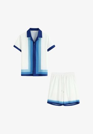 Chemise blanche à manches courtes avec col bleu et rayures bleues en dégradé, associée à un short blanc avec bordure en dégradé bleu assortie.