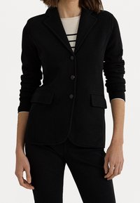 Černý blazer v přesně střiženém designu, který obsahuje dvě přední kapsy, tři knoflíky a límec. Vyroben z měkké, strukturované tkaniny.