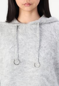 Grå, fluffig hoodie med dragsnodd och silverfärgade metalldetaljer. Mjuk textur, avslappnad design och en ledig passform.