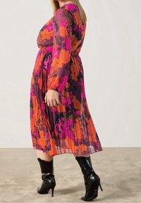 Robe longue plissée en tissu transparent, avec un imprimé floral dans des tons vifs de rose, orange et violet. Manches longues et taille élastique.
