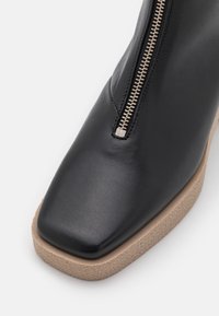 Sort ankelstøvle i læder med firkantet tå, sidelås og lysfarvet tekstureret sål. Glat finish med minimale detaljer.