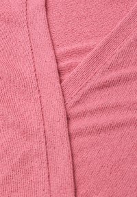 Gros plan sur un tissu tricoté rose doux montrant un col côtelé et un motif tricoté texturé.