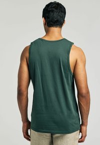 Mørkegrøn bomulds tanktop med brede ærmehuller, en rund halsudskæring og en afslappet pasform, vist fra ryggen mod en neutral baggrund.