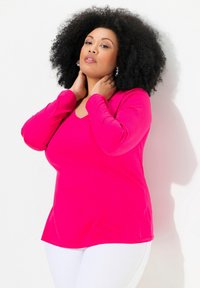 Fuchsiová dlouhá halenka s výstřihem do V, měkkou texturou a uvolněným střihem, spárovaná s bílými kalhotami.