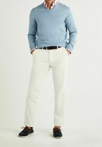 Jasnoniebieski sweter z dekoltem w serek, białe spodnie i czarne sznurowane buty. Sweter ma ściągacze na rękawach; spodnie są proste z paskiem.