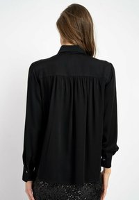 Czarna bluzka z długim rękawem, z zapięciem na guzik przy mankiecie, miękka tkanina, plisowany design z tyłu i kołnierz, połączona z cekinową spódnicą.