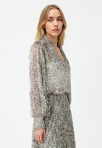 Blouse met luipaardprint met lange pofmouwen, een zijdeachtige textuur en een kraag; gecombineerd met een bijpassende rok in hetzelfde patroon.