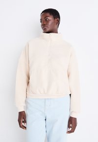 Cremfarbener Fleece-Pullover mit hohem Kragen, halblangem Reißverschluss und elastischem Saum. Mit strukturierten Ärmeln und einem einfarbigen unteren Abschnitt.