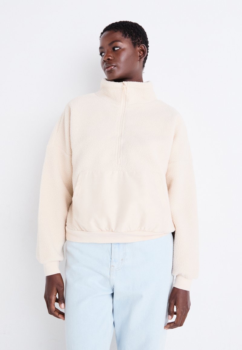 Cremfarbener Fleece-Pullover mit hohem Kragen, halblangem Reißverschluss und elastischem Saum. Mit strukturierten Ärmeln und einem einfarbigen unteren Abschnitt.