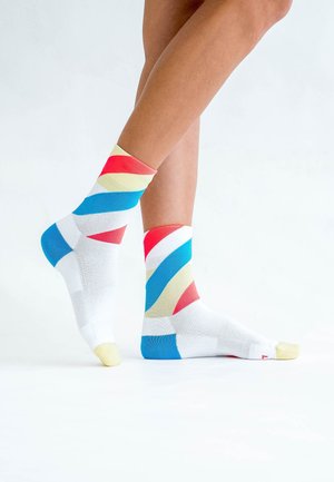 Bunte Sneakersocken mit weißem Grund, die geometrische Muster in Rot, Blau, Gelb und Weiß zeigen. Strukturierter Strickstoff.