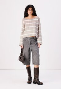 Beige stickad tröja med vita ränder, grå vida jeans och knähöga bruna läderstövlar. Modellen håller en liten brun väska.