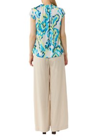 Blumenbluse mit kurzen Kappärmeln in Blau, Grün und Weiß. Kombiniert mit beigen weitem Hosen. Weicher, leichter Stoff.
