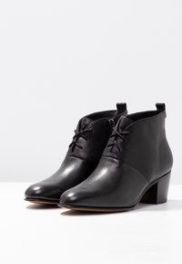 Botas negras hasta el tobillo que presentan una puntera de cuero liso, parte trasera texturizada, cordones en la parte delantera y un tacón bajo para un soporte estable.