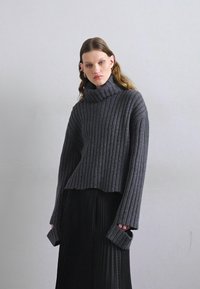 Suéter de gola alta, em cinza escuro e com textura canelada, com um corte descontraído e mangas longas, combinado com uma saia preta plissada a condizer.