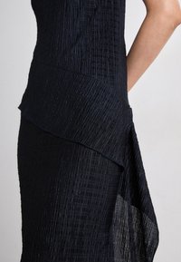 Black textured dress with layered ruffle detail. Fabric appears lightweight and slightly sheer with a crinkled pattern.