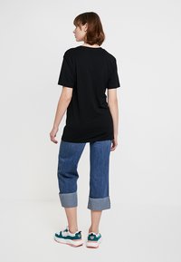 Sort kortærmet t-shirt med en afslappet pasform, parret med cropped blå jeans med opkrøllede manchetter og farverige sneakers.