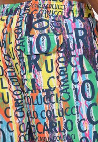 Mehrfarbige Shorts mit dichten Textmustern in Schwarz und lebendigen Farben, mit einer aufgesetzten Tasche an der Seite und einem elastischen Bund.