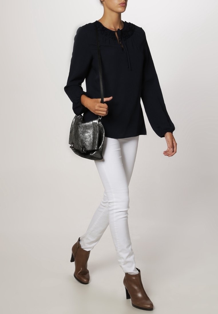 Námořnická blůza se sešitým výstřihem a detailem na zavázání, kterou modelka kombinovala s bílými úzkými džíny a hnědými kotníkovými botami. Modelka nese kovovou kabelku.