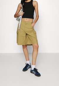 Shorts cargo kaki avec deux poches latérales et une coupe décontractée, associés à un crop top noir et des baskets bleu marine avec des rayures bleues.