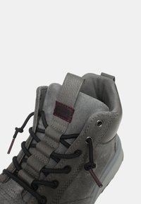 Scarpa alta in suede grigio con lacci rotondi, linguetta testurizzata, etichetta a strappo e suola in gomma. Presenta un piccolo dettaglio con logo sul lato.
