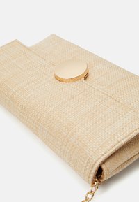 Beige texturovaná kabelka s klapkou, která má zlaté kulaté zapínání a řetízek, navržena pro všestranné použití.