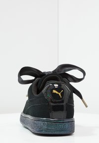 Baskets Puma noires avec semelle scintillante, lacets en ruban de satin surdimensionné et logo Puma doré sur le talon brillant.