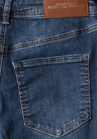 Mörkblå denimjeans med en bakficka med dekorativ sömnad och en rektangulär läderlapp märkt "Street One - Denim Atelier."