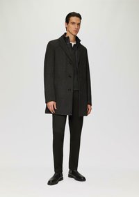 Donkergrijs wollen jasje met een gestructureerde afwerking, twee voorkruiden en drie knopen, gecombineerd met zwarte broek en leren enkellaarzen.