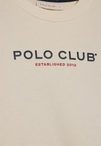 Sweatshirt in off-white stof, met een ronde halslijn. Voorzijde tekst in marineblauw: "POLO CLUB," met "ESTABLISHED 2012" in rood eronder.