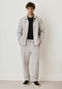 Light gray athletic tracksuit featuring a zip-up jacket with a collar and drawstring pants. Paired with black sneakers. Smooth texture.