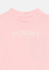 Roosa puuvillane T-särk ümmarguse kaelusega, millel on keskelt veidi tõstetud valge kiri "TOMMY HILFIGER".