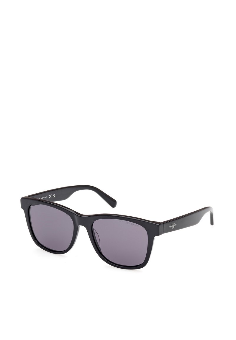 Gafas de sol negras con montura cuadrada, lentes ahumados grises y acabado mate. Presentan un logo sutil en la patilla y brazos elegantes y rectos.