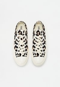 Tenisky s leopardím potiskem v černé a béžové barvě na béžovém plátně, s bílými gumovými podešvemi a kovovými oky.
