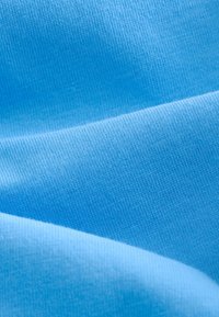 Svetlo modro bombažno blago z gladko teksturo, ki vsebuje fin rebrasti vzorec in mehke gube, kar poudarja njegovo prožnost in padajočo obliko.