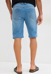 Shorts en denim bleu clair avec une coupe droite et des poches cousues, finition avec un ourlet propre. Portés avec des sandales noires.